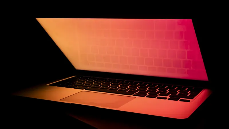 A half-open laptop glowing orange and pink in a dark room